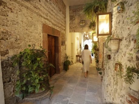 A guest walks through a stone corridor of the San Miguel house, among hanging plants and warm light