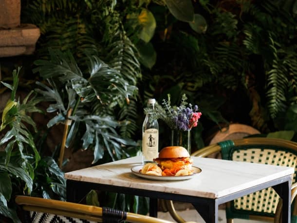 A marble table on Aura's terrace, with a sandwich, a bottled drink and flowers, among ferns