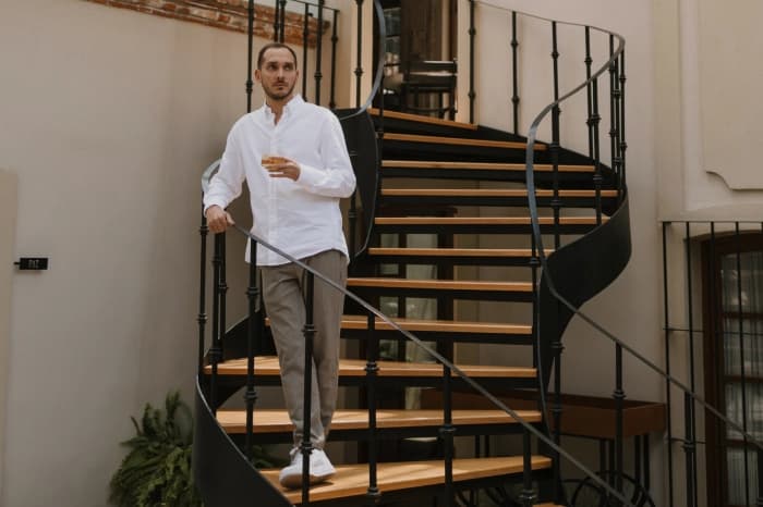 Someone coming down the courtyard's wood-and-iron spiral stair, a glass in hand