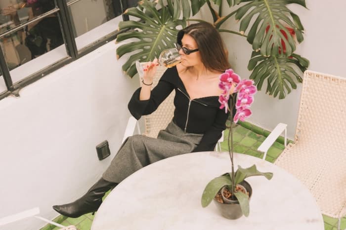 Someone seated on the terrace with a glass of white wine, beside a marble table with an orchid and a monstera leaf behind