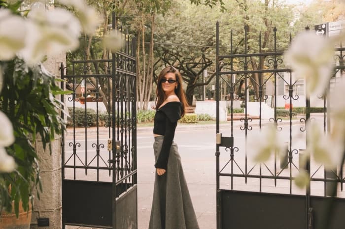 Someone standing at the Polanco house's wrought-iron gate, the tree-lined street behind and white orchids blurred in the foreground