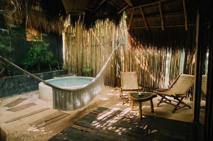 A hammock strung in front of the terrace's round tub, wooden chairs and timber walls under the palm roof