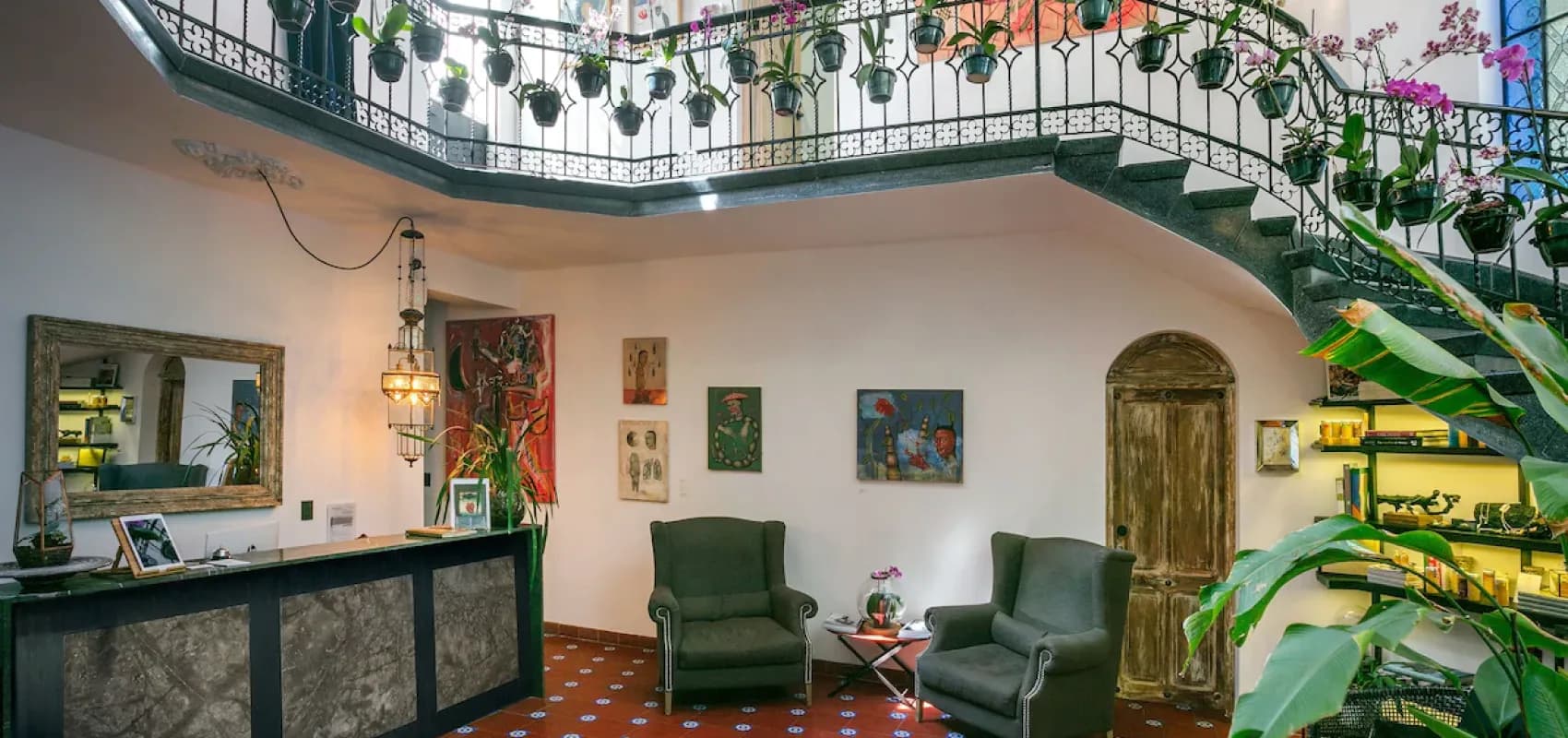 The Polanco lobby seen head-on: the front desk, green armchairs and the wrought-iron staircase with hanging orchids beyond
