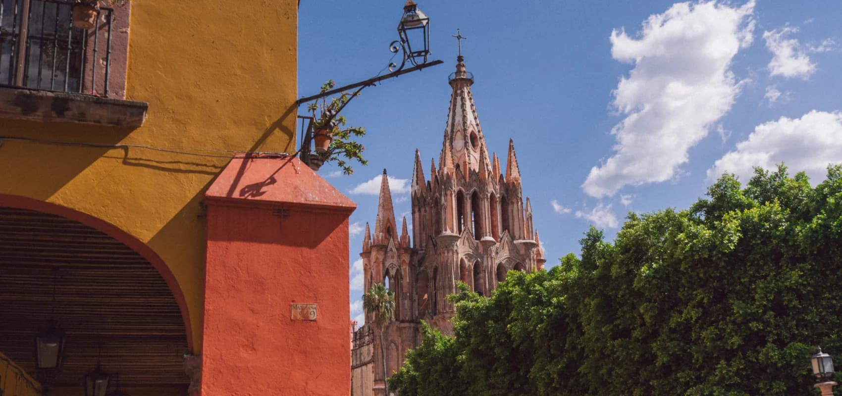 La Parroquia's pink towers among colorful colonial facades and an iron lamp, against a blue sky
